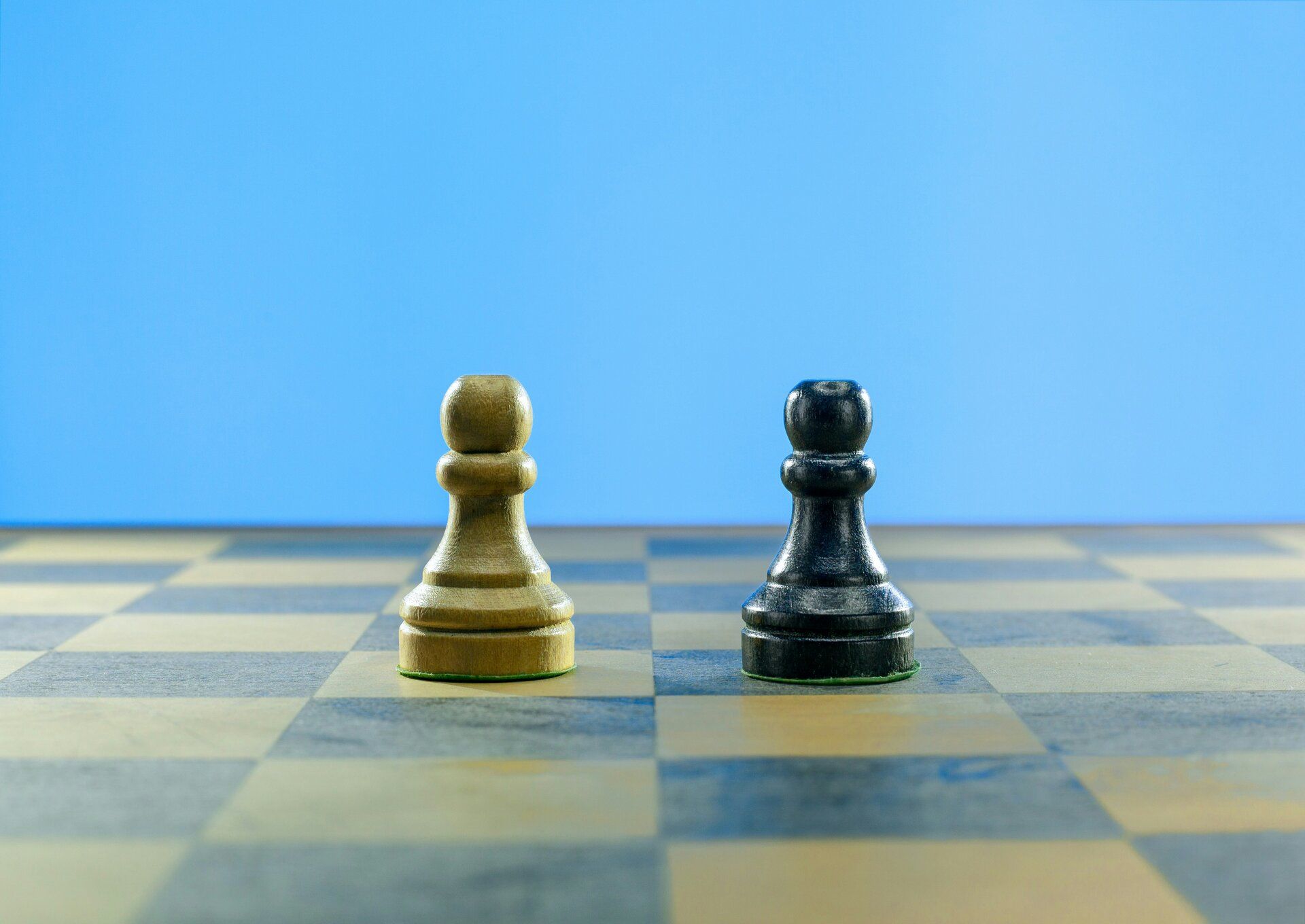 A light and a dark wooden pawn side by side on a chessboard.